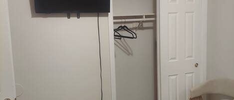A room with a flat-screen TV mounted on the wall, a door leading to a closet, and a chair near the door.