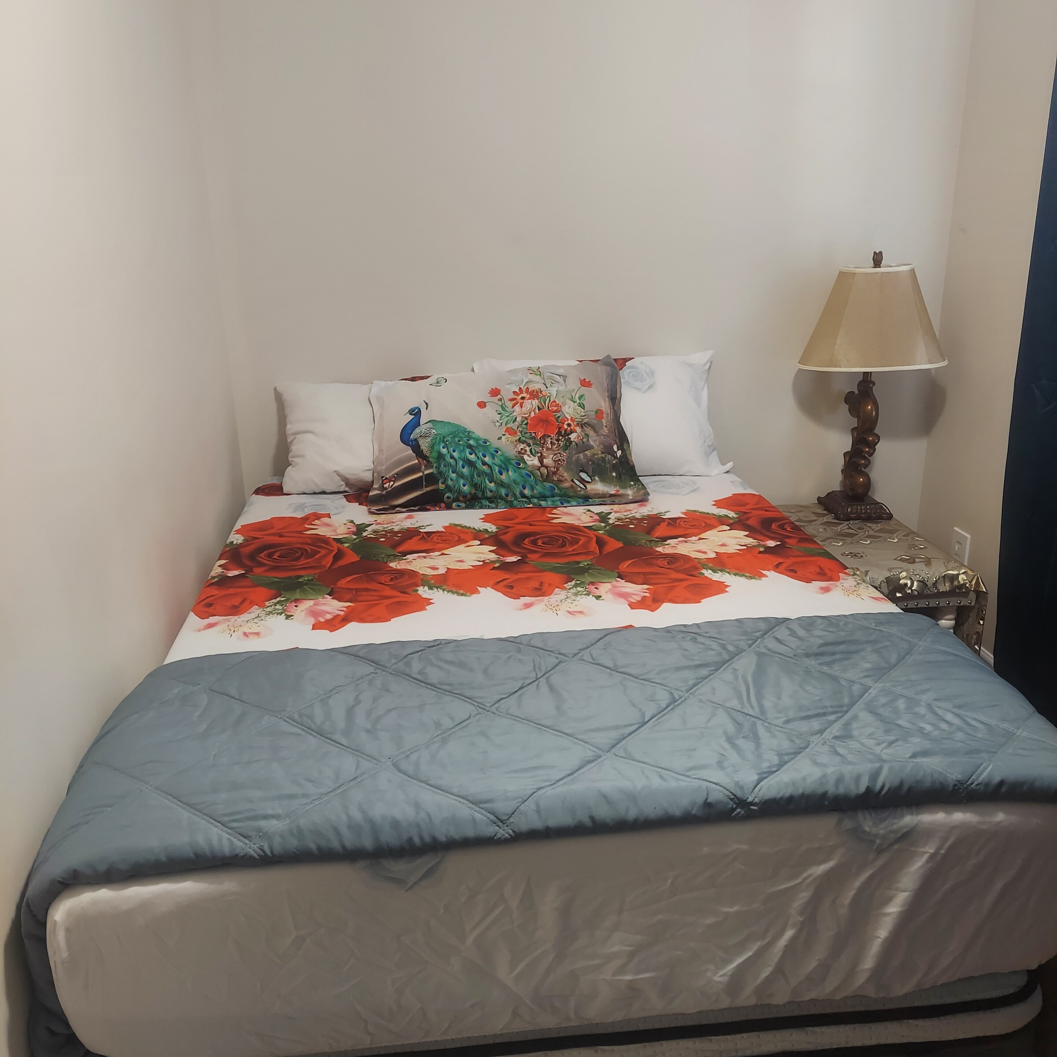 A bed with a floral quilt, a peacock pillow, and a lamp beside it.