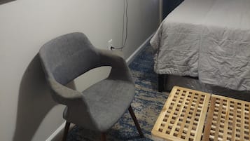 A hotel room with a bed, a chair, a television mounted on the wall, and a painting on the wall.
