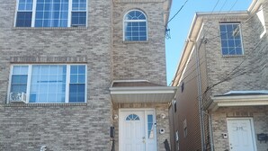 A two-story brick building with a white front door, a garage, and a staircase leading to the entrance. - Crystal Room (Newark)