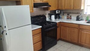 A kitchen with wooden cabinets, a white refrigerator, a black stove, and a coffee maker. - Crystal Room (Newark)
