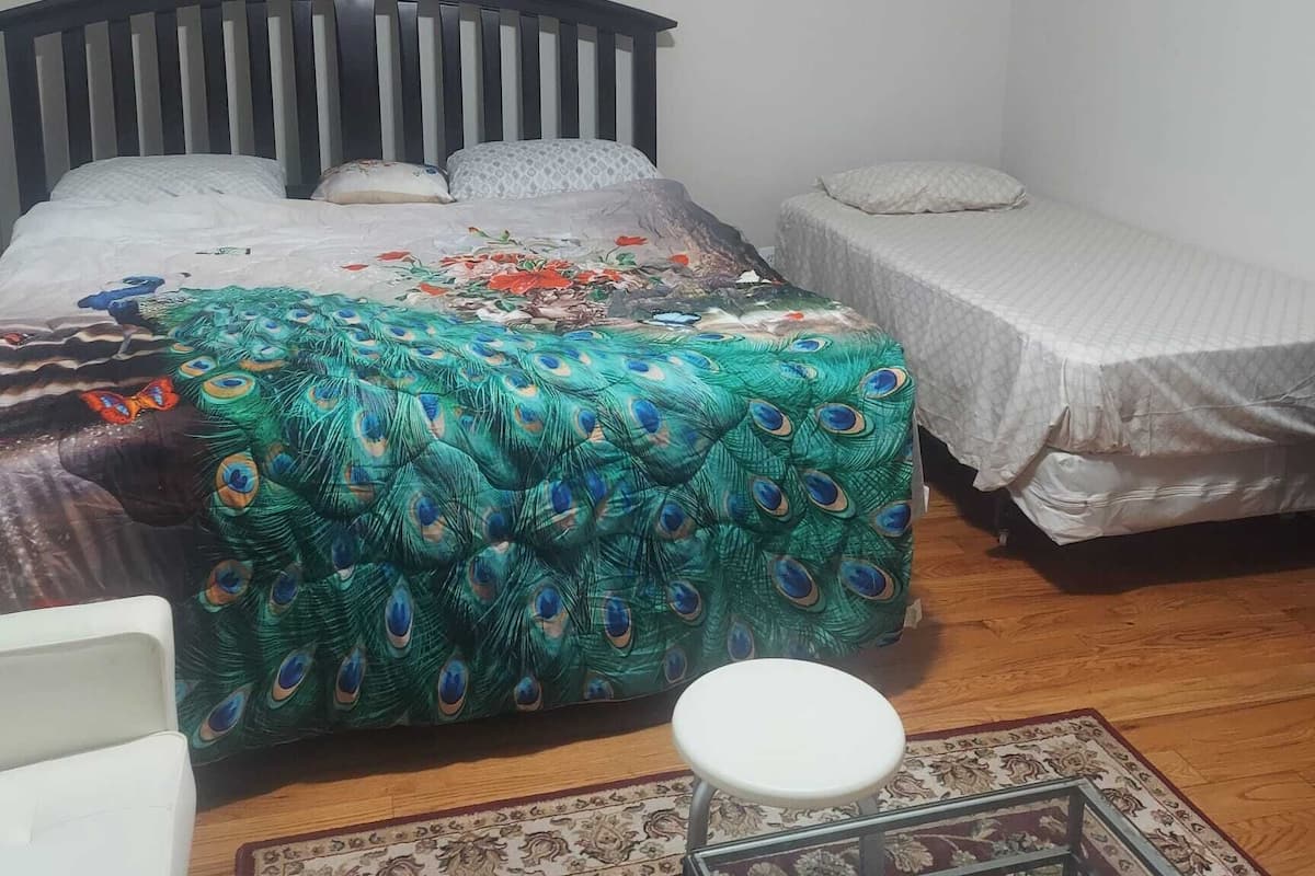 A bedroom with a bed, a smaller bed, a chair, a framed picture on the wall, and a radiator.