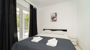 A bedroom with a bed, black curtains, a white headboard, a white wall, and a framed picture of a flower. - Beautiful apartment in Pridraga with WiFi (Pridraga)