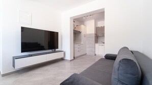 A modern living room with a flat-screen TV, grey sofa, and a kitchen area with white cabinets and a countertop. - Beautiful apartment in Pridraga with WiFi (Pridraga)
