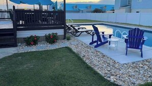 Un jardin avec une piscine, une terrasse et du mobilier d’extérieur.