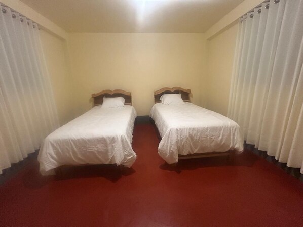 Una habitación con dos camas individuales, alfombra roja y cortinas blancas.