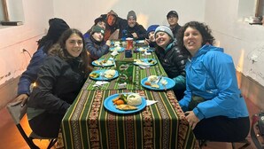 A group of people seated around a long dining table with a patterned tablecloth, plates of food, and a water bottle.