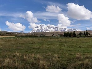 A mountainous landscape with a grassy field and scattered buildings. - Casa Cóndor Ausangate (Ocongate)