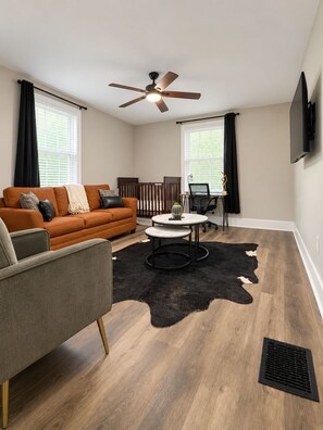 A modern living room with a sofa, a coffee table, a ceiling fan, and a television mounted on the wall. - Optimum - Uptown Oasis (Birmingham)
