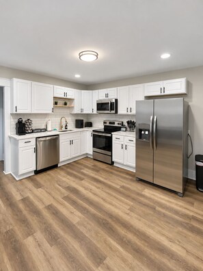 A modern kitchen with white cabinetry, stainless steel appliances, and a wooden floor. - Optimum - Uptown Oasis (Birmingham)