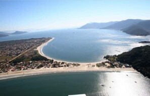 Vista aérea de una zona costera con una playa, un pueblo a lo largo de la costa y montañas al fondo.