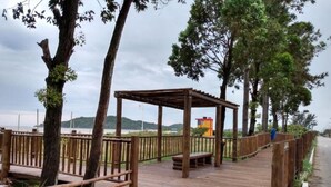 Eine Holzterrasse mit einer Pergola, umgeben von Bäumen und einem Zaun, mit Blick auf ein Gewässer.