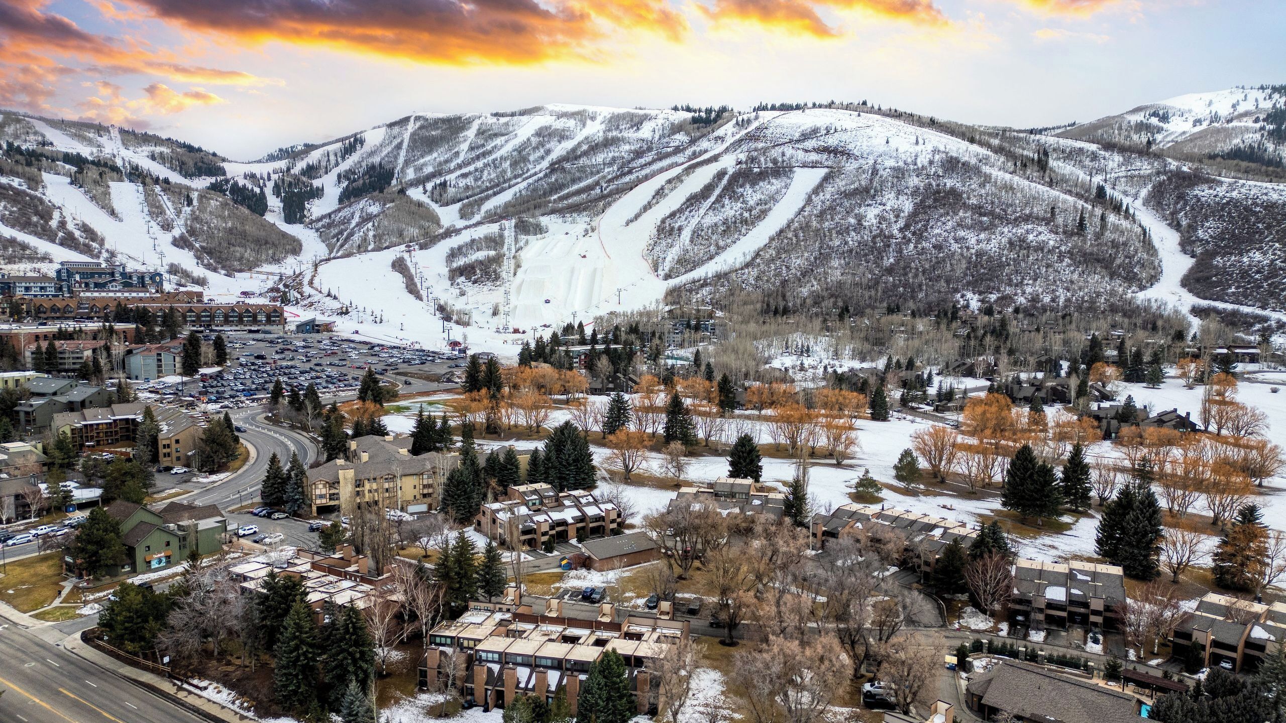 A town with snow-covered hills, buildings, and a parking lot.