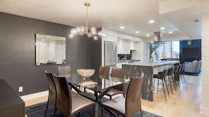 A modern kitchen with a central island, a dining area with a glass table and leather chairs, and a living area with a fireplace.