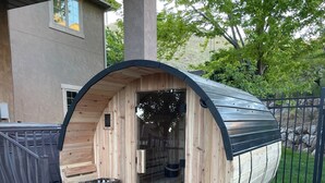 A wooden barrel-shaped structure with a bench and a basket inside, placed on a stone base with a metal fence nearby. - Beautiful, New 2-bedroom Sundance Retreat (Orem)