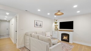 A modern living room with a sectional sofa, a fireplace, a flat-screen TV, and a ceiling light fixture. - Beautiful, New 2-bedroom Sundance Retreat (Orem)