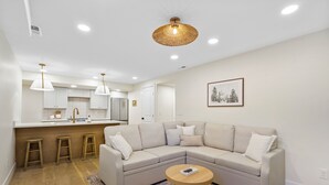 A modern living room with a beige sectional sofa, a round coffee table, and a kitchen area in the background. - Beautiful, New 2-bedroom Sundance Retreat (Orem)