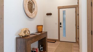 A hallway with a wooden console table, a mirror, a skull decoration, a vase, and a door with a frosted glass panel. - 1-bedroom + Den, Elk Creek Luxury Condo G301 (Fraser)