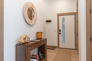 Un pasillo con una consola de madera, un espejo, una decoración de calavera, un jarrón y una puerta con panel de vidrio esmerilado.