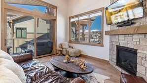 A modern living room with a fireplace, large windows, and a leather sofa. - 1-bedroom + Den, Elk Creek Luxury Condo G301 (Fraser)