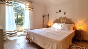 Un dormitorio con cama, dos lámparas de noche, una escalera de madera y vistas a árboles a través de una ventana.