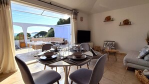 Un comedor con una mesa dispuesta para cuatro personas, un sofá y un televisor en una habitación con vistas al exterior.