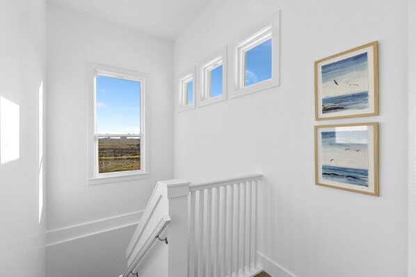 Una habitación con una pared blanca, un radiador blanco y tres cuadros enmarcados que muestran paisajes marinos.