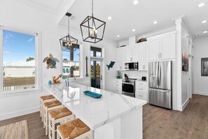 Una cocina moderna con armarios blancos, una isla central con taburetes, electrodomésticos de acero inoxidable y vistas al exterior.