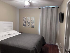 Ein Schlafzimmer mit einem Bett, einem Deckenventilator, einem Fenster mit Vorhängen und Wandbildern.