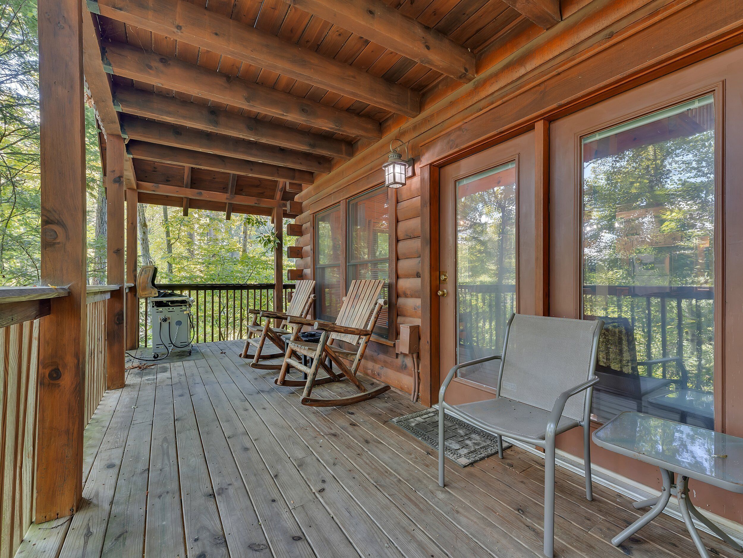 Une terrasse en bois avec des fauteuils à bascule et une table, donnant sur une zone boisée.