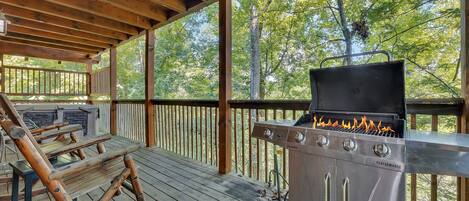 An outdoor deck with a barbecue grill, wooden benches, and a stone fireplace.