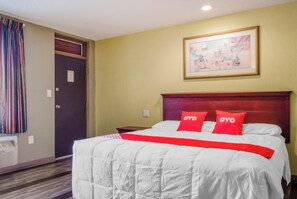 A hotel room with a large bed, a headboard, a framed picture on the wall, and a door with curtains.