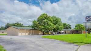 A building with a green roof, a parking lot, and a tree in front. - OYO Budget Inn Bartow (Bartow)