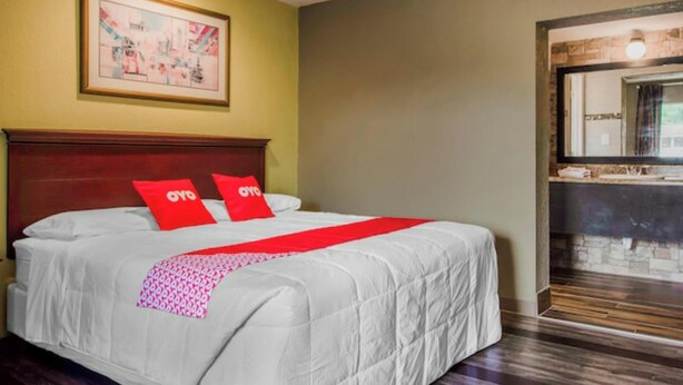 A hotel room with a large bed, a wooden headboard, a red throw blanket, and a framed picture on the wall. - OYO Budget Inn Bartow (Bartow)