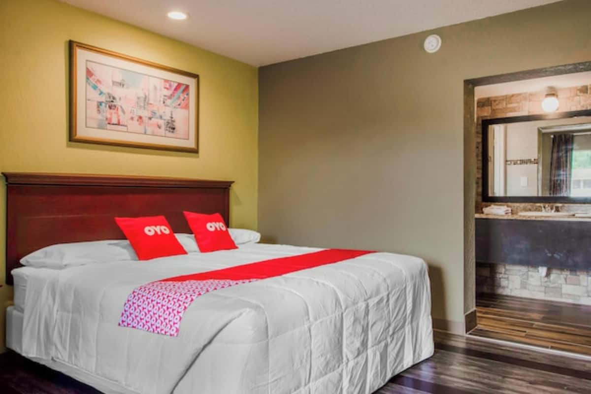 Quarto de hotel com uma cama grande, cabeceira de madeira, manta vermelha e um quadro na parede.