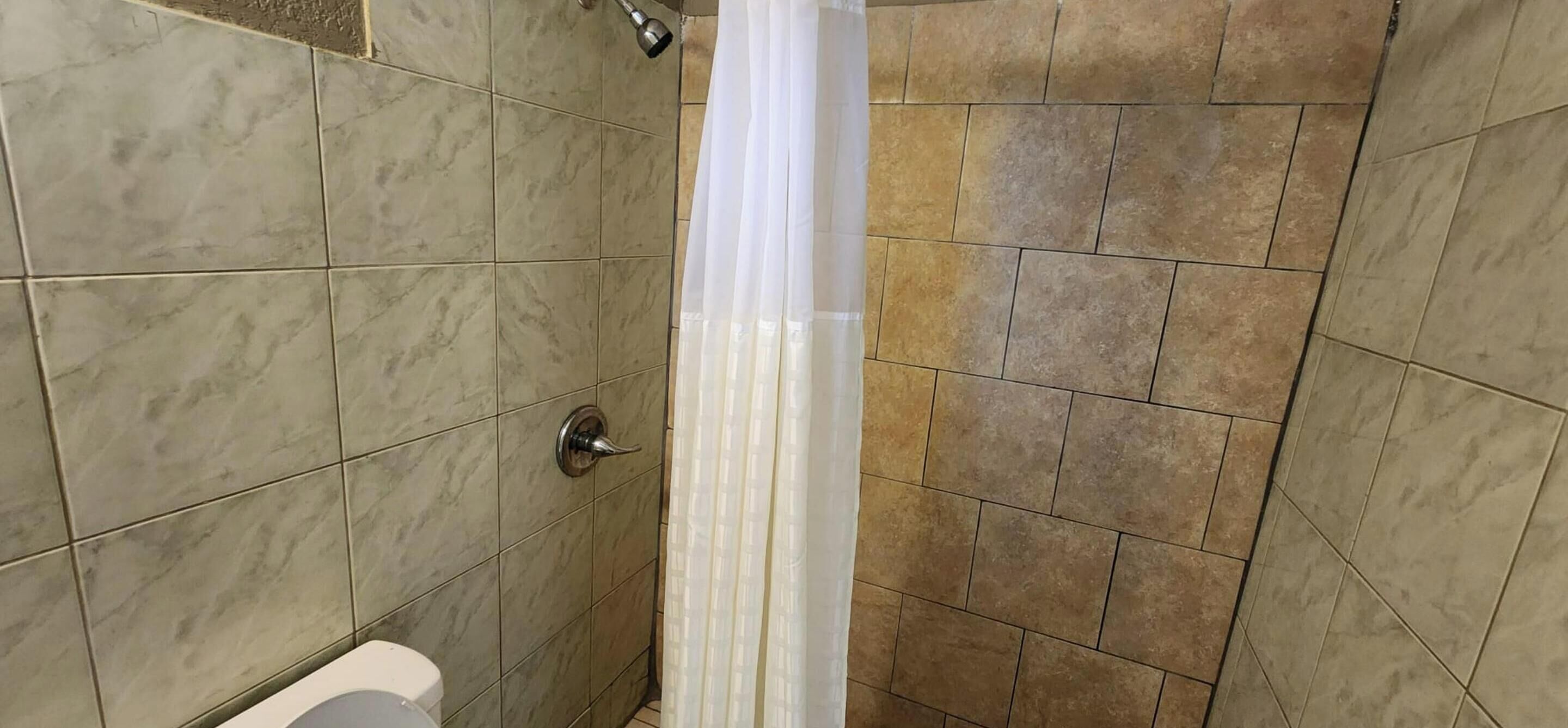 A bathroom with a shower, tiled walls, a toilet, and a curtain.