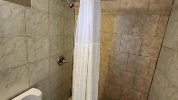 A bathroom with a shower, tiled walls, a toilet, and a curtain.