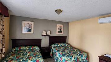 Quarto de hotel com duas camas, uma mesa de cabeceira, uma luminária e um aparelho de ar condicionado.