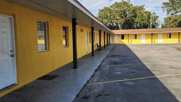 A row of yellow motel rooms with white doors and windows, a covered walkway, and a parking lot.