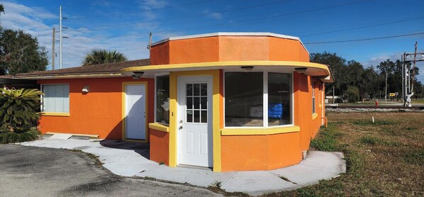 A small, single-story building with a curved corner design, a white door, and large windows.
