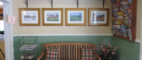 A reception area with a wooden bench, framed pictures on the wall, a shelf with baskets, and a bulletin board with pamphlets.