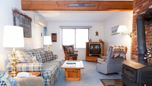 En hyggelig stue med sofa, lænestole, et træsofabord, fjernsyn og en murstenspejs.