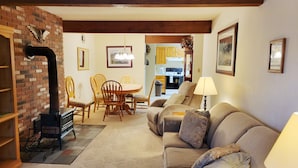A cozy living room with a fireplace, a sofa, a dining table with chairs, and a kitchen in the background. - Official Seasons RMC Condo 21C - 2 bedrooms - sleeps 8 - No Fees (Bartlett)