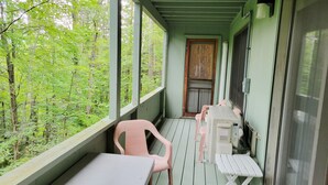 A covered porch with a table and chairs, a door, and a view of a forested area. - Official Seasons RMC Condo 21C - 2 bedrooms - sleeps 8 - No Fees (Bartlett)