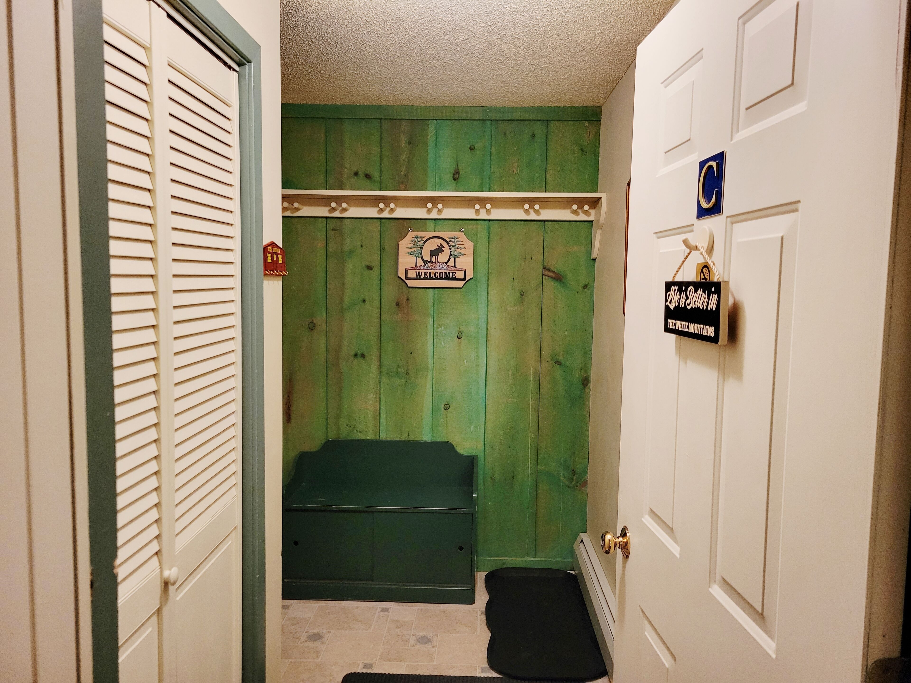 A narrow hallway with a green door, a bench, and a welcome sign.