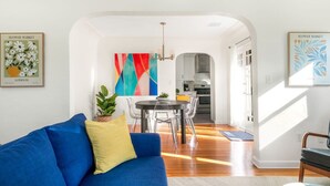 A modern living room with a blue sofa, a dining table with chairs, and a kitchen in the background. - 3 Bed Home, A/C, Parking, Big Yard in Heart of SD (San Diego)