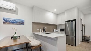 Une cuisine moderne avec des meubles blancs, un réfrigérateur en acier inoxydable et un petit îlot central doté d’un évier.
