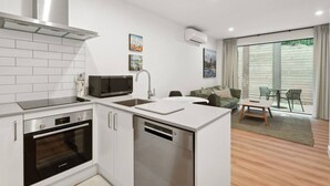 Eine moderne Küche mit weißen Schränken, einem Bosch-Backofen und einem Geschirrspüler. Es gibt einen Essbereich mit Tisch und Stühlen sowie ein großes Fenster mit Vorhängen.