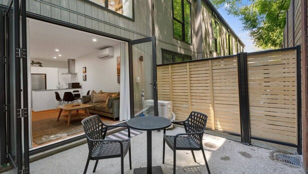 Ein modernes Haus mit Glastür, die zu einem Wohnbereich mit einer Couch, einem Esstisch und Stühlen führt.