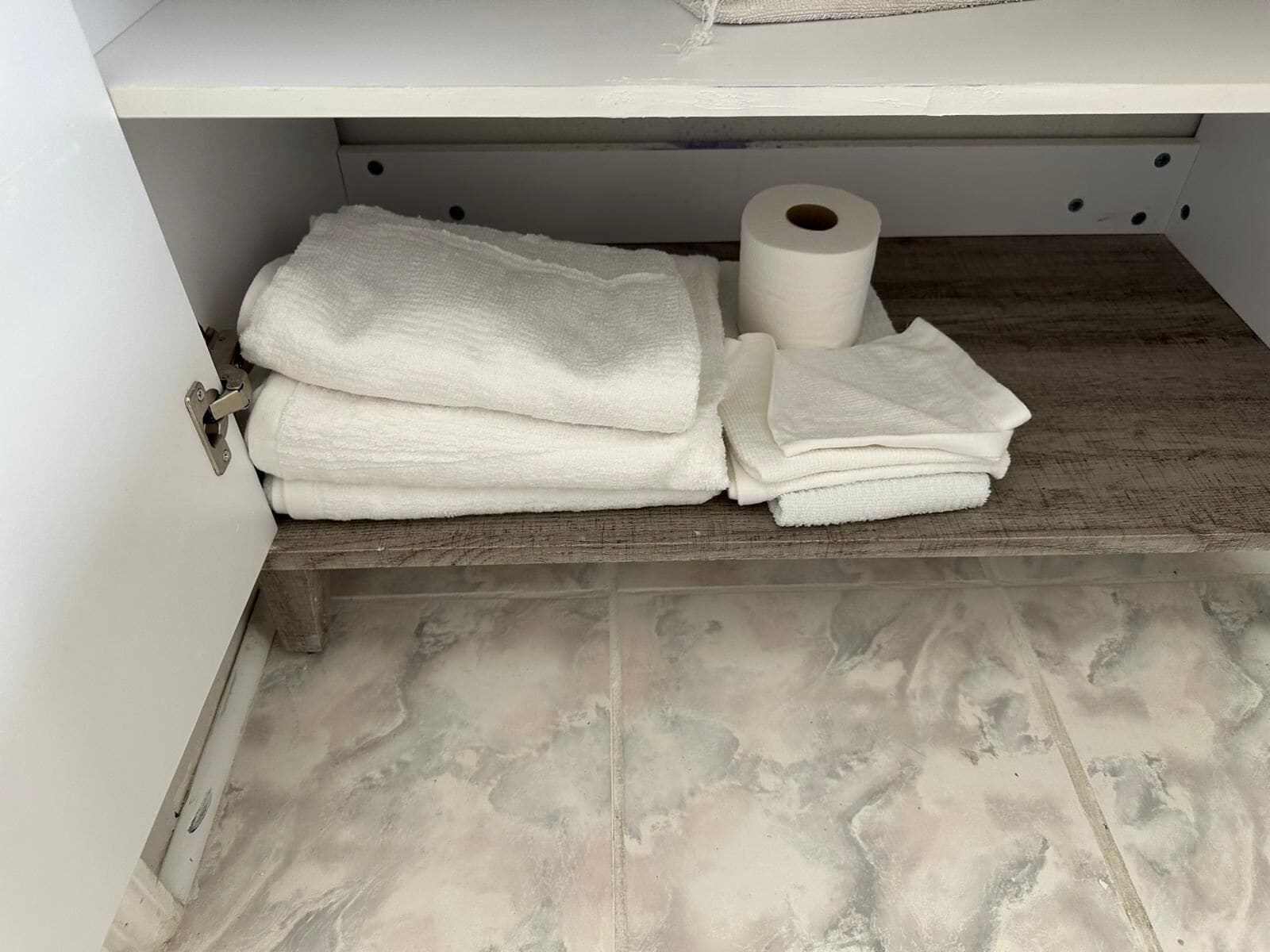 Un baño con un lavamanos blanco, un perchero con toallas dobladas y un rollo de papel higiénico.